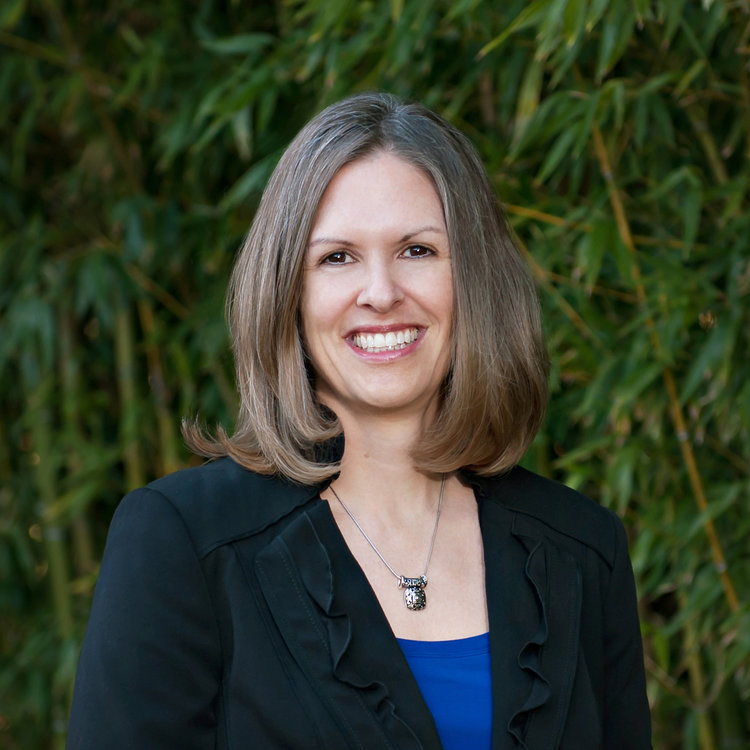 A smiling woman in a black blazer and blue blouse providing strategic consulting in the tech industry.