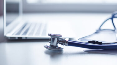 A stethoscope on a desk next to a laptop in a strategic company.