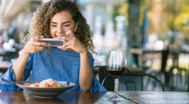 A woman strategically capturing her delicious food with the help of modern technology at a table.